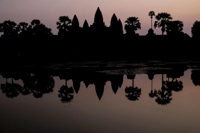 Silhouette of Angkor Wat's towers and palm trees reflected in a still pool at dawn in Siem Reap