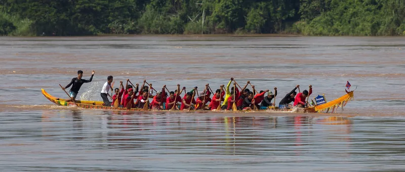 Rowers in red paddle a long racing pirogue across the Mekong River in Si Phan Don, Laos.