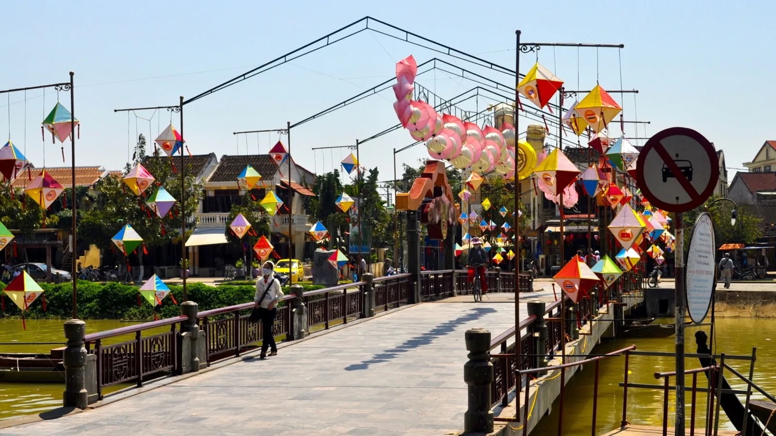 Colorful paper lanterns and dragon decorations hang over a bridge crossing the river in Hoi An's Old Town.