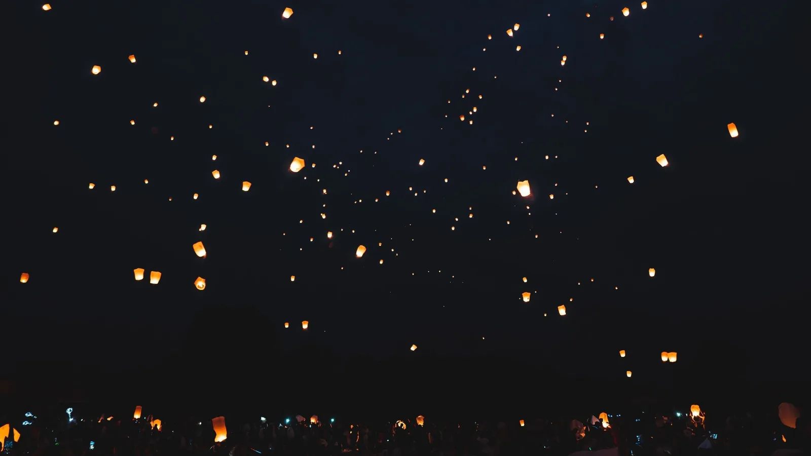 Glowing sky lanterns drift upward into the dark night during a festival in Thailand.