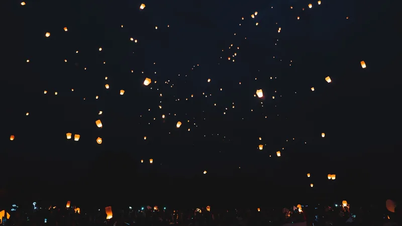 Glowing sky lanterns drift upward into the dark night during a festival in Thailand.